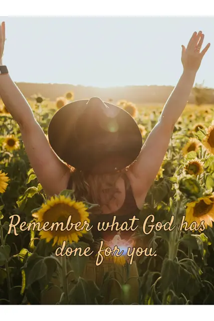 A woman in a black hat walks through a field of sunflowers, with her hands raised toward the sun. Remember what God has done for you.