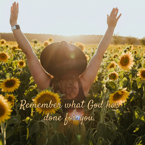 A woman in a black hat walks through a field of sunflowers, with her hands raised toward the sun. Remember what God has done for you.